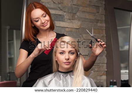 Happy young woman getting new haircut by hairdresser at parlor. redhead hairdresser cutting client\'s hair in beauty salon