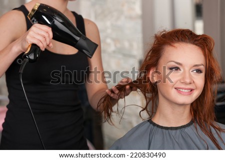 closeup on stylist hands drying redhead woman hair in salon. Young female giving new hair style to woman at parlor
