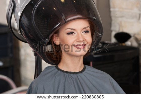 happy redhead women drying under hairdryer. Portrait of woman under hairdressing machine in parlor