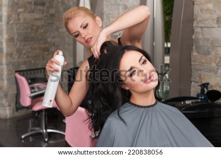 Young female hairdresser applying spray on client\'s hair. Female hairdresser works on woman hair in salon