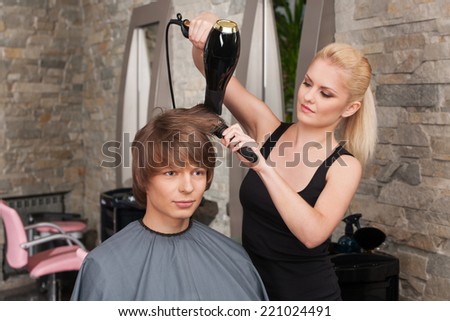 Blond female hairdresser drying hair of man client. young attractive man sitting in hair salon