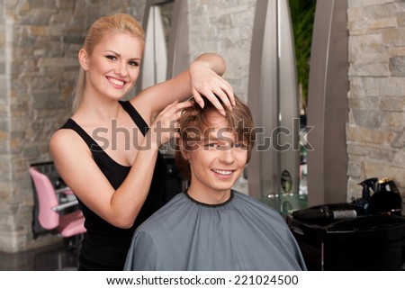 blond hairstylist applying hair mousse spray. young attractive man sitting in hair salon