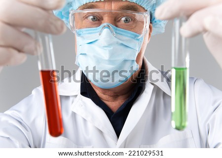 closeup of surprised man wearing mask looks at test tubes. adult scientist holding test tubes on white background