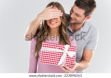Man surprising his girlfriend with gift on grey background. man covering eyes of girl and standing behind
