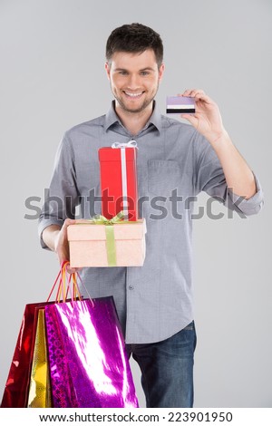 man holding bagsand boxes with credit debit card. young happy excited guy holding credit card on grey