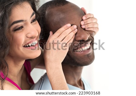 young girl covering her boyfriend eyes with both hands. Young woman covering african black man eyes