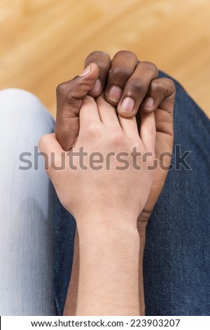 Close up of couple holding hands while sitting. top view of woman putting her hand on african man hand