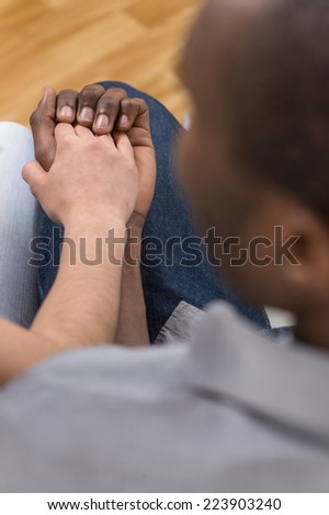 Close up of couple holding hands while sitting. over shoulder view of woman putting her hand on african man hand