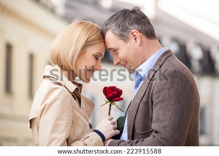 Portrait of two people holding rose and smiling. adult man giving red flower to blond woman outside