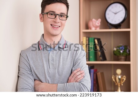 portrait of handsome young man smiling indoor. guy wearing glasses looking into camera with bookshelves on background