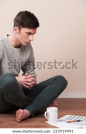 young man sitting on floor with legs crossed. handsome guy reading documents and drinking on wooden floor