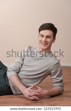 young casual man sitting and smiling to the camera. guy lying on floor and leaning inside home
