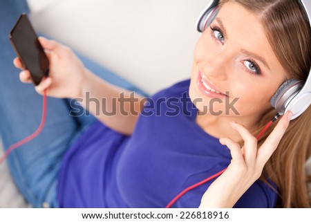 beautiful young girl listens to music on headphones. happy woman with headphones resting on sofa and looking into camera