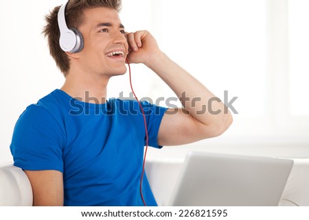 Happy man in headphones with laptop relaxing on sofa at home. handsome guy using laptop and resting while singing song