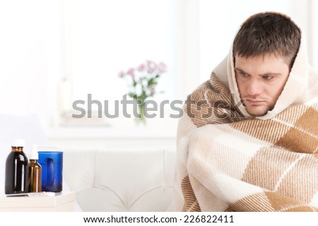 young man sitting on sofa covered with blanket. sick man looking tired and ill looking at bottles