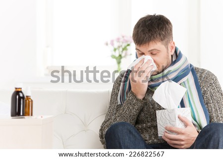 Man blowing his nose in his living room. closeup on guy sitting on sofa and sneezing