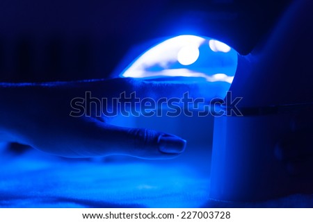 Manicure in process using Uv lamp for nails. client woman drying nails at manicurist salon in dark