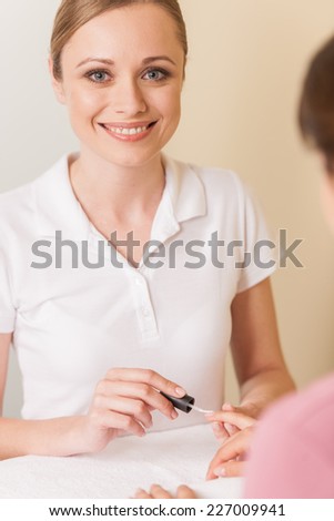Close-up of beautician hand painting nails of woman in salon. manucurist women sitting in spa salon and looking at camera
