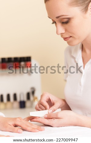 Close-up Of Beautician Hand Filing Nails Of Woman In Salon. manucurist women sitting in spa salon and looking at fingers
