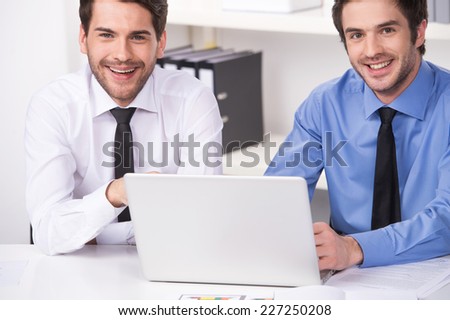 two businessmen having discussion in office. two smiling businessmen looking at camera with laptop