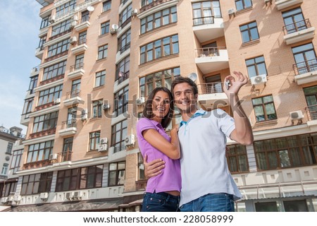 Couple in front of new home holding door keys. man hugging womam and holding apartment keys
