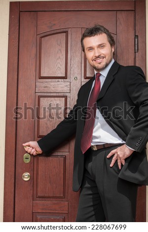 realtor opening wooden door and smiling. brown wooden door and business man in suit and tie