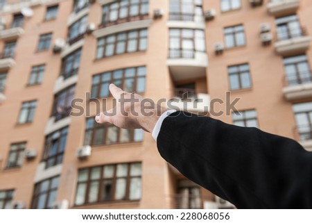 businessman hand pointing in direction of apartment. Real estate agent shows new apartment in tall building