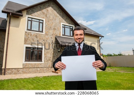 closeup on smiling real estate agent ready to sell house. Male real etate agent in front of home holding blank card
