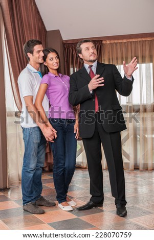 man real estate agent showing hugging couple new house. male agent showing view from new house window