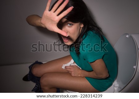 Portrait of young woman shouting in toilet to camera. top view of scared black-haired girl lifted hands and hiding from camera