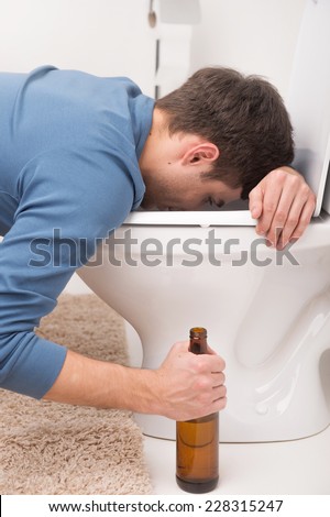 Drunk man sleeping on toilet and holding bottle. sick man is vomiting and feeling bad