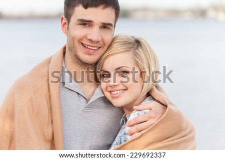 Attractive young couple standing on beach at summer. happy woman and man standing under blanket and smiling