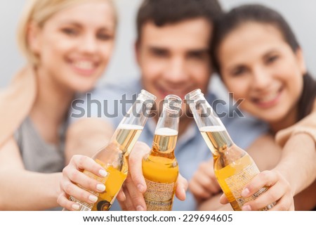 Man and two women relaxing on beach with beer. Happy friends drinking together on beach with focus on bottle