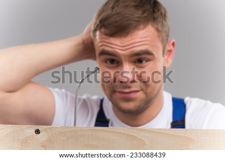 Man having difficulty getting nail hammered into wood. guy thinking and looking at bent nail on grey background
