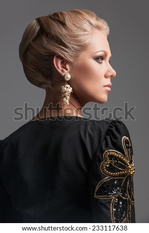 back view of beautiful blonde woman looking away. delicate blonde girl with jewelry standing on grey background