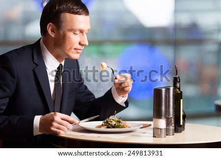 Handsome man eating at restaurant inside. side view of man sitting on chair in cafe and eating food
