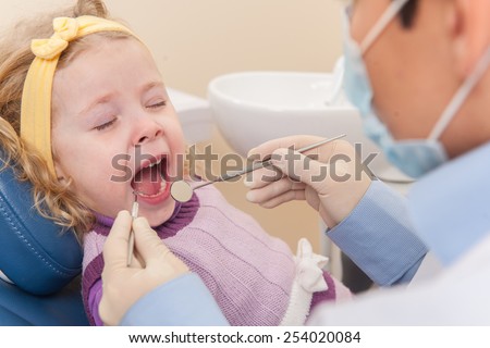 crying girl at dentist opened mouth. man dentists examining one girl in dentist chair