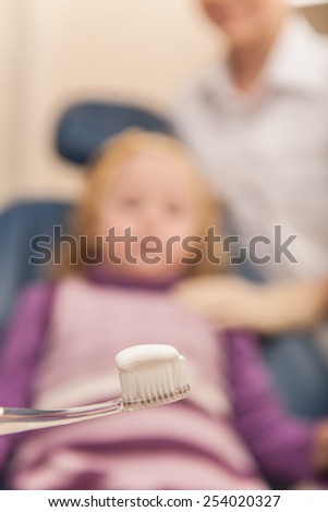 Dentist showing girl how to brush her teeth. closeup on toothbrush with tooth paste and woman on background
