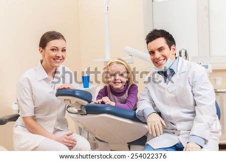 Little girl at dentist looking up and smiling. man and woman dentists examining one girl
