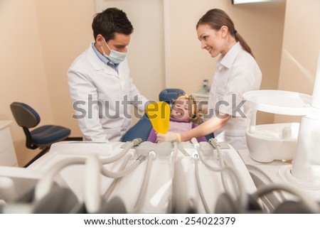 woman holding mirror and showing girl her teeth. dental office and little girl patient sitting in chair