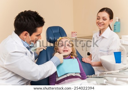 Little girl at dentist looking up and smiling. man and woman dentists examining one girl