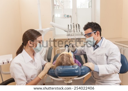 back view of little girl at dentist chair. man and woman dentists examining one girl in dentist chair