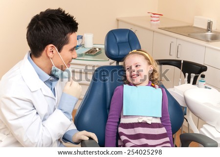 Little girl is having her teeth examined by dentist. dentist talking to smiling girl in chair