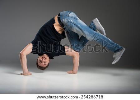 young break dancer showing his skills on grey background. Hip hop dancer man performing isolated over dark background