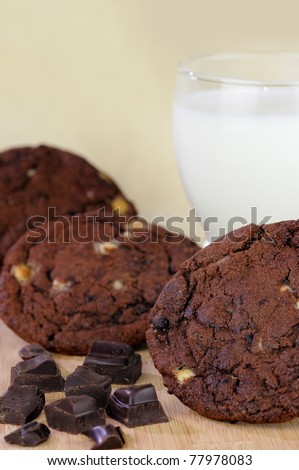 Chocolate chip cookies with a glass of milk and chocolate pieces on a beige background with a shallow DOF.