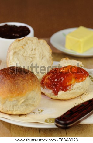 A bread roll cut in half in a layout with butter and strawberry jam.