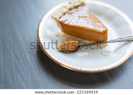 Pumpkin pie on a white china plate with gold detailed rim and antique silver dessert fork.