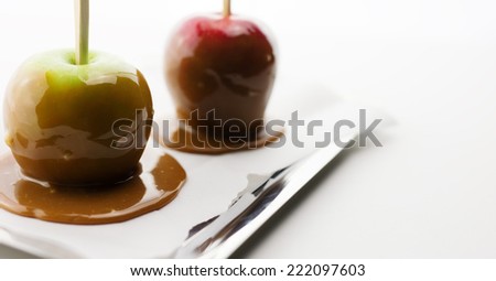 Red and green caramel apples on silver tray with parchment paper and chop sticks against white background.
