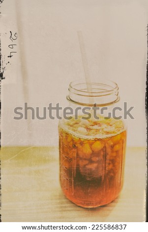 Iced tea in a jar with ice and a straw on a wooden board against a brightly lit background.