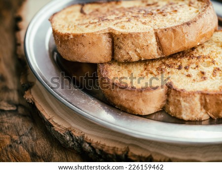 Two pieces of French toast on a silver plate and wooden board.